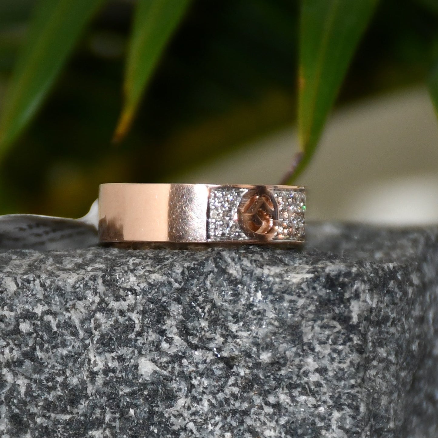 A 14kt gold diamond band ring with smaller diamonds, set on a gold band displayed on a rough textured surface.