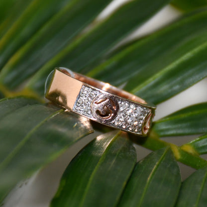 A 14kt gold diamond band ring with smaller diamonds, set on a gold band displayed on a green leaf.