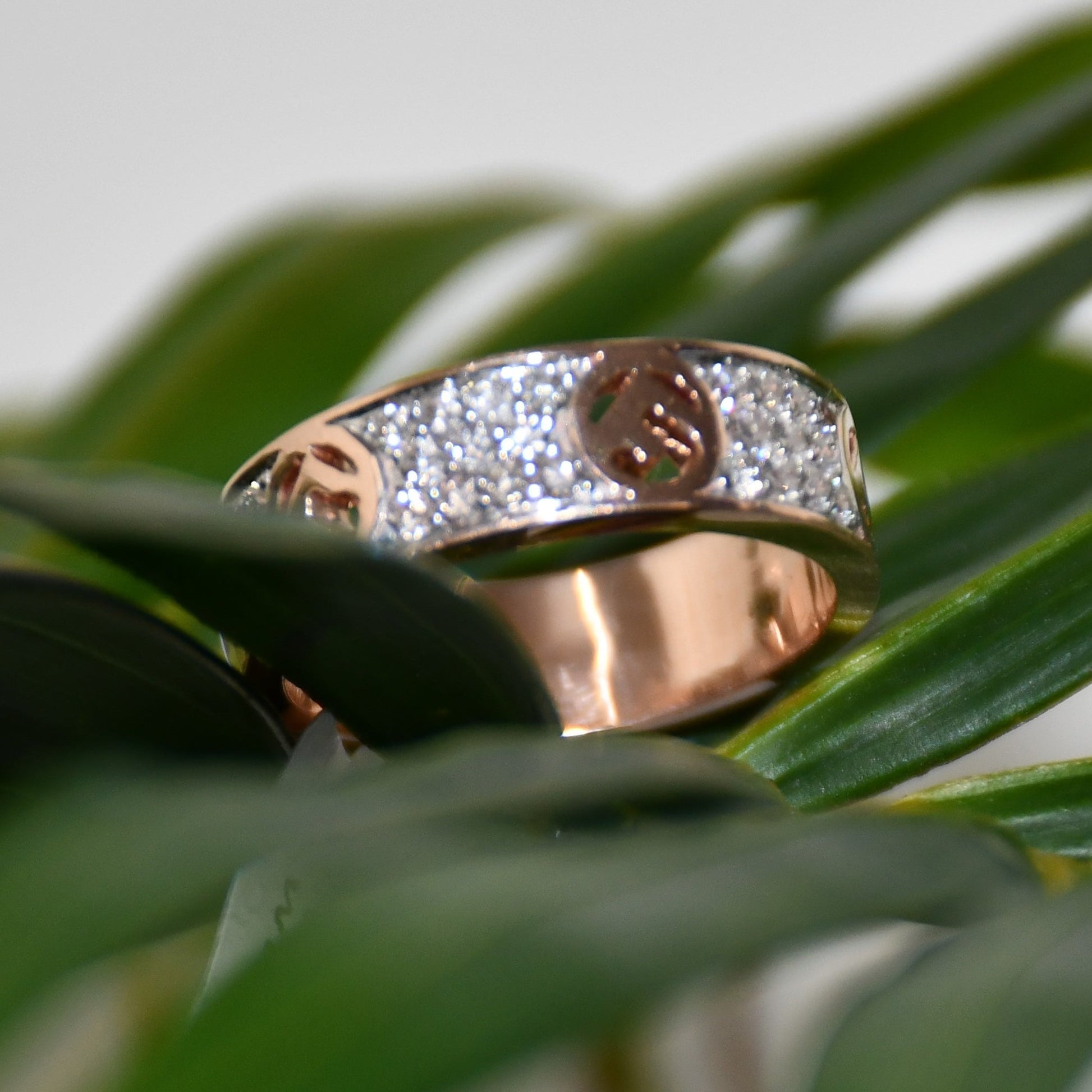 A 14kt gold diamond band ring with smaller diamonds, set on a gold band displayed on a green leaf.