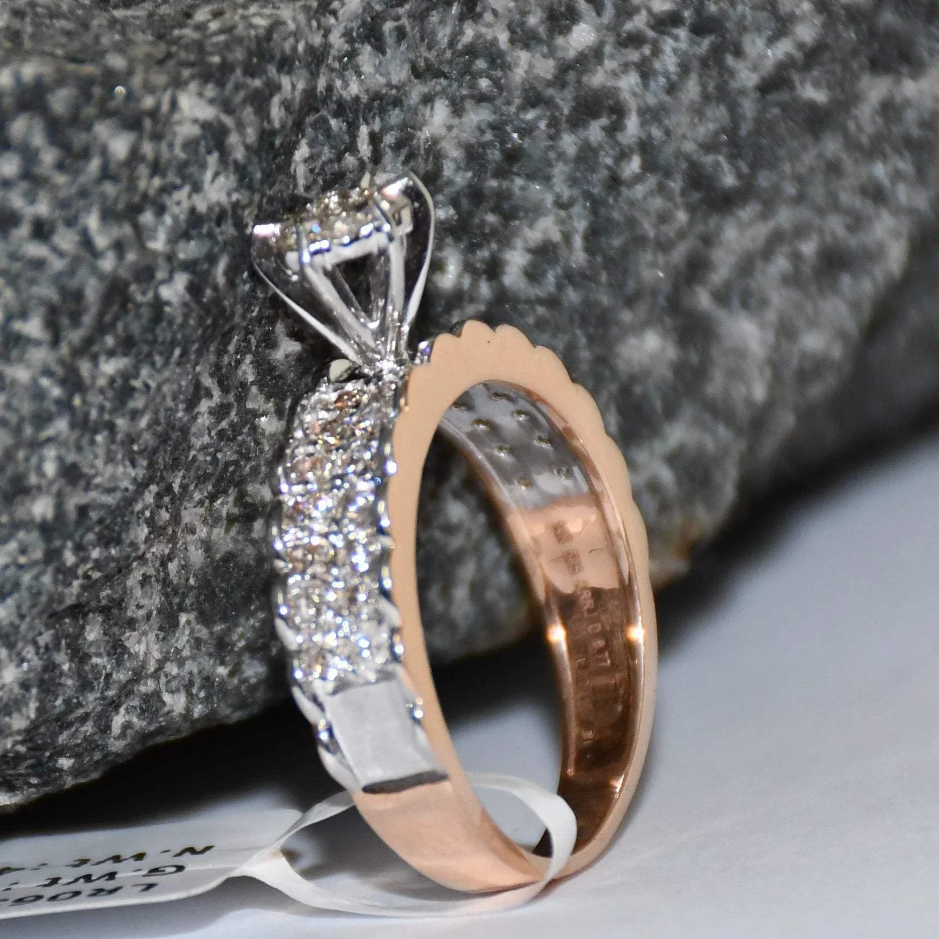 A 14K gold diamond band ring with a clear, certified diamond centerpiece displayed standing against a black and grey rough background.