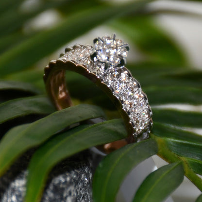 A 14K gold diamond band ring with a clear, certified diamond centerpiece displayed with green leaves surface.