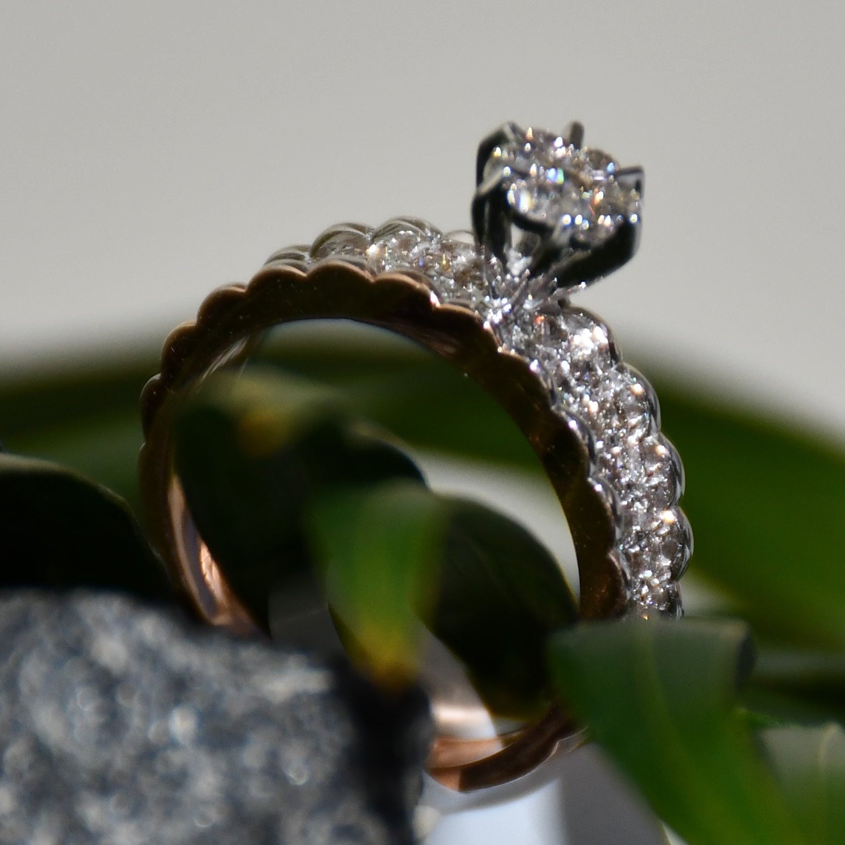 A 14K gold diamond band ring with a clear, certified diamond centerpiece displayed standing against a black, grey and green background.
