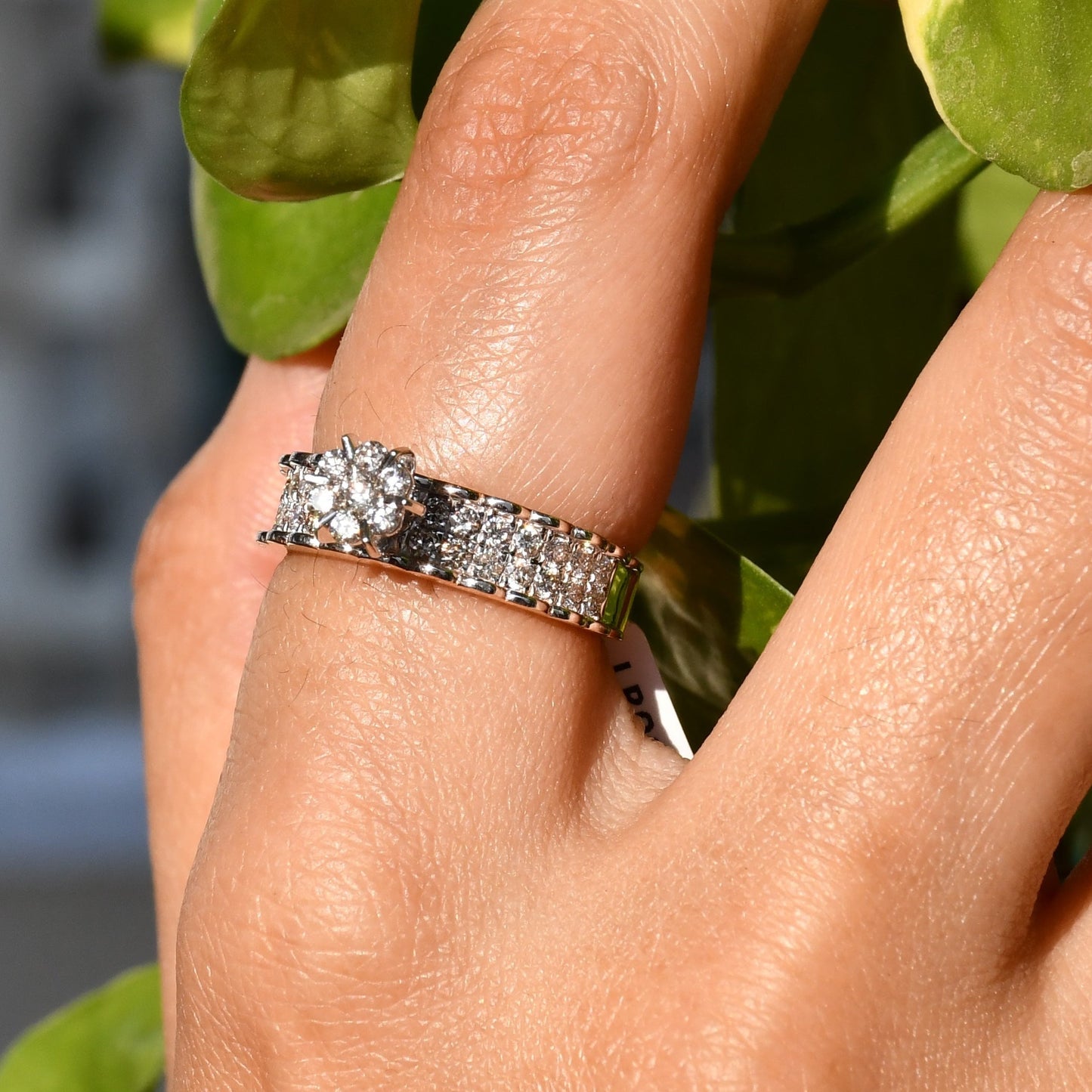 A person's hand holding a 14K gold diamond band ring with a clear, certified diamond centerpiece.