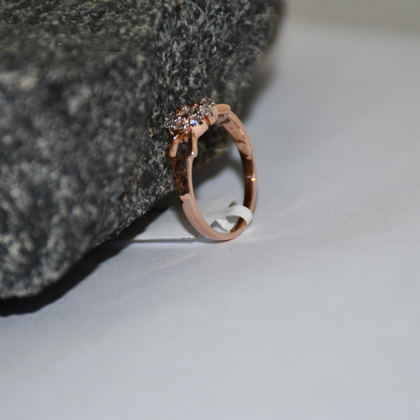 A 14K gold diamond band ring with a central row of diamonds and smaller surrounding diamonds set in a gold band displayed on a white surface with the support of a rough black stone.