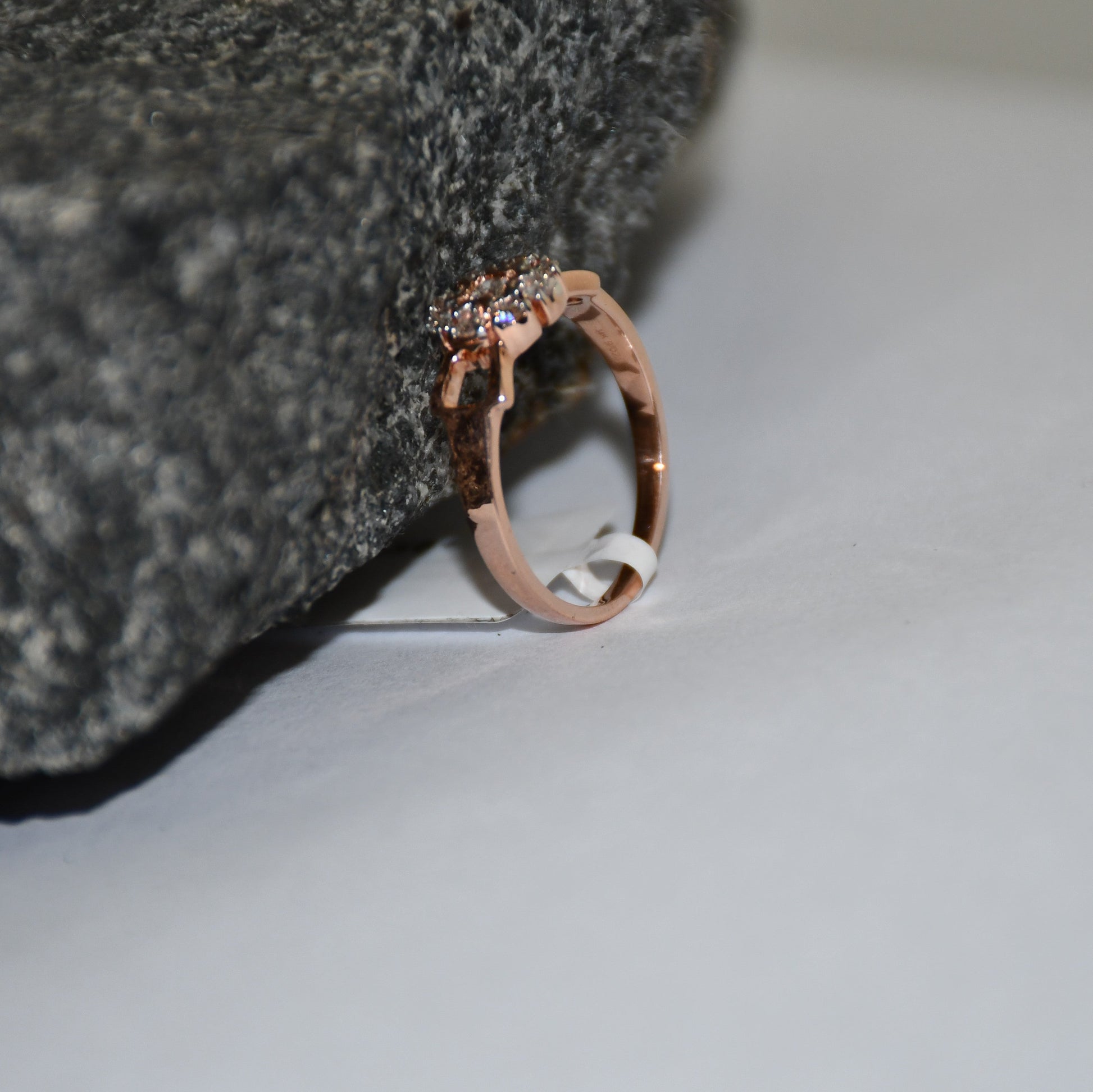 A 14K gold diamond band ring with a central row of diamonds and smaller surrounding diamonds set in a gold band displayed on a white surface with the support of a rough black stone.