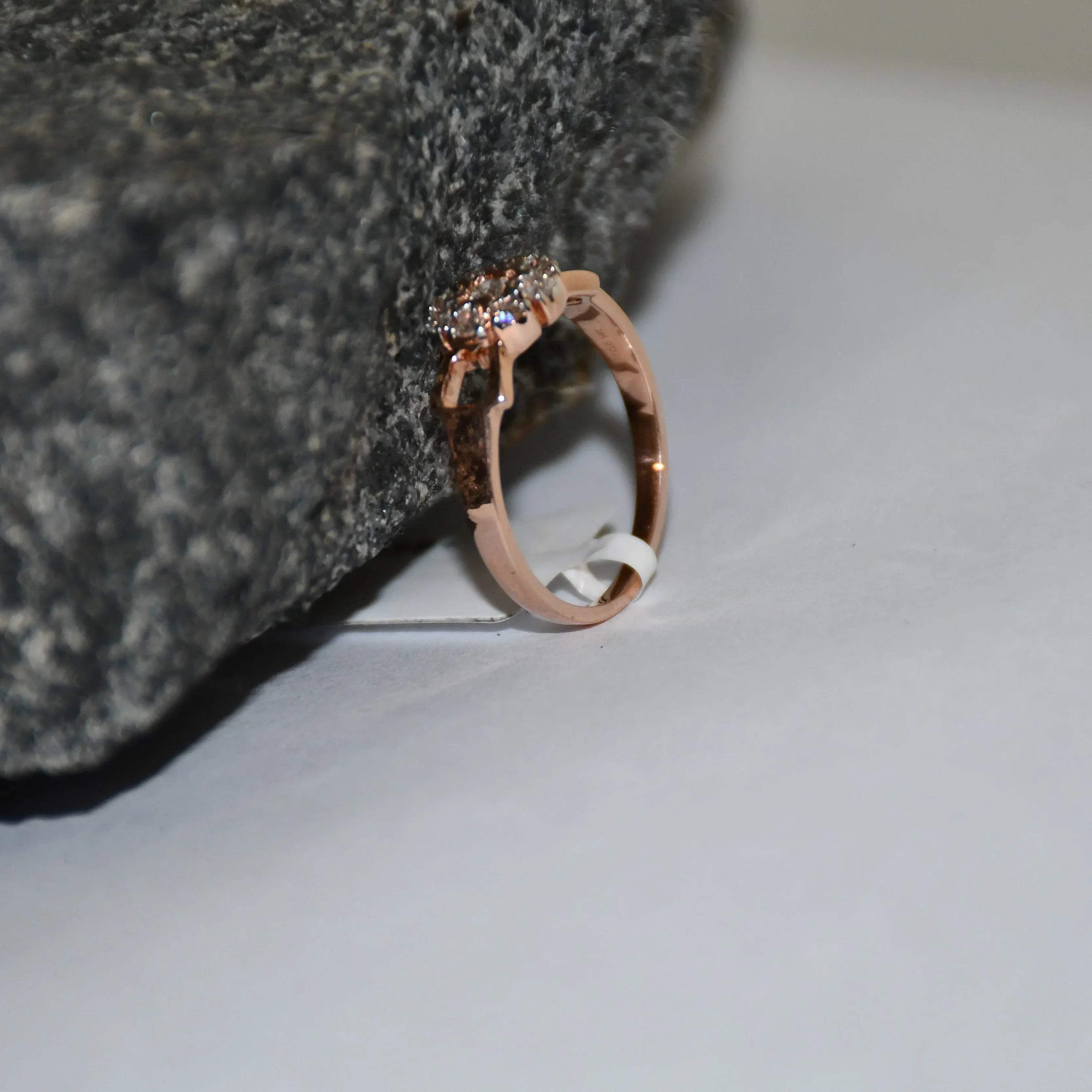 A 14K gold diamond band ring with a central row of diamonds and smaller surrounding diamonds set in a gold band displayed on a white surface with the support of a rough black stone.