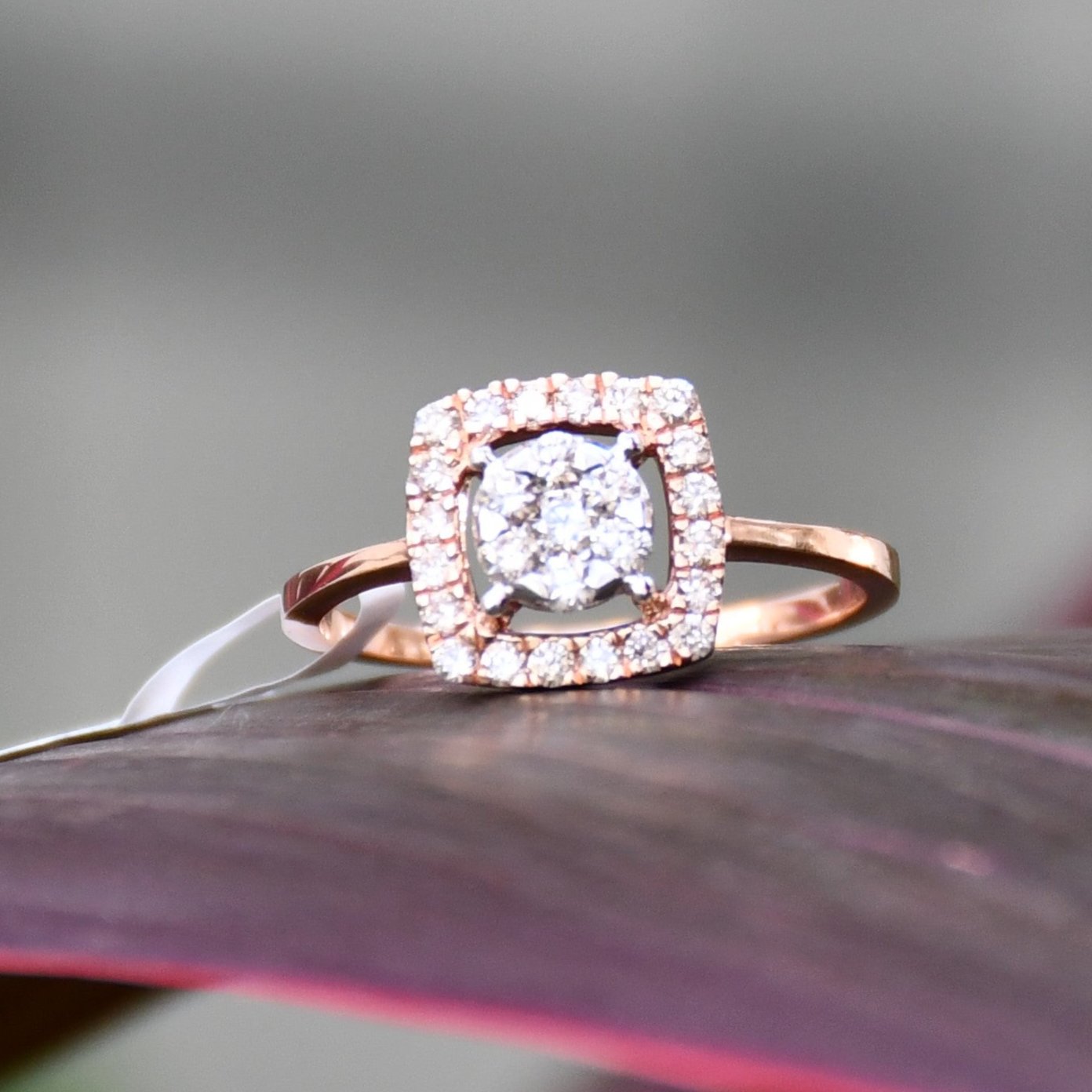 A gold band ring with a square-shaped, brilliant-cut diamonds centerpiece, set on a red surface.