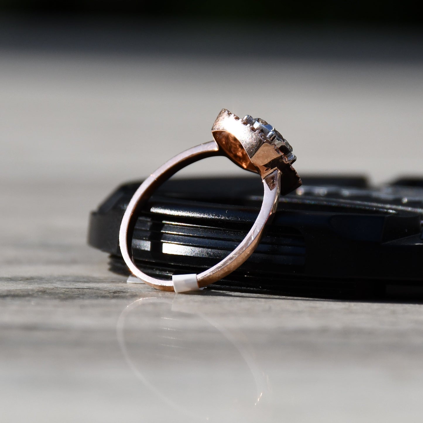 A gold band ring with a square-shaped, brilliant-cut diamonds centerpiece, set on a black surface.