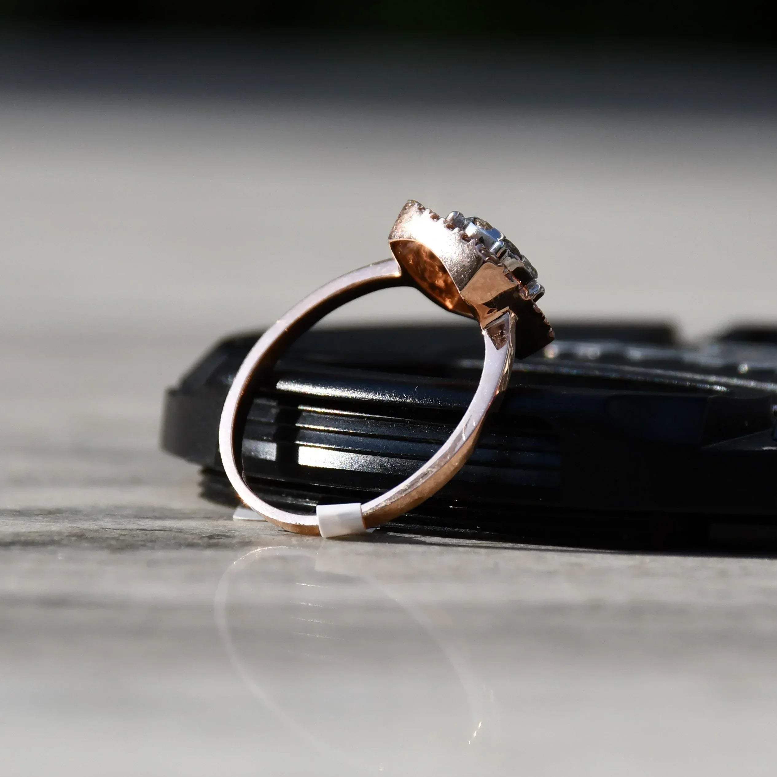 A gold band ring with a square-shaped, brilliant-cut diamonds centerpiece, set on a black surface.