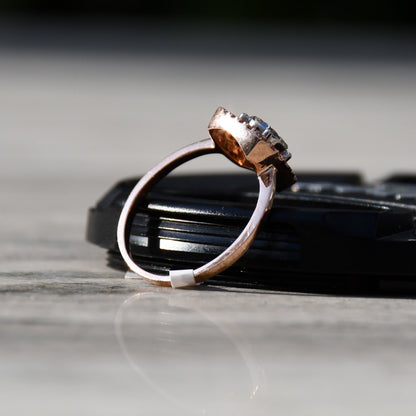 A gold band ring with a square-shaped, brilliant-cut diamonds centerpiece, set on a black surface.