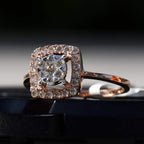 A gold band ring with a square-shaped, brilliant-cut diamonds centerpiece, set on a black surface.