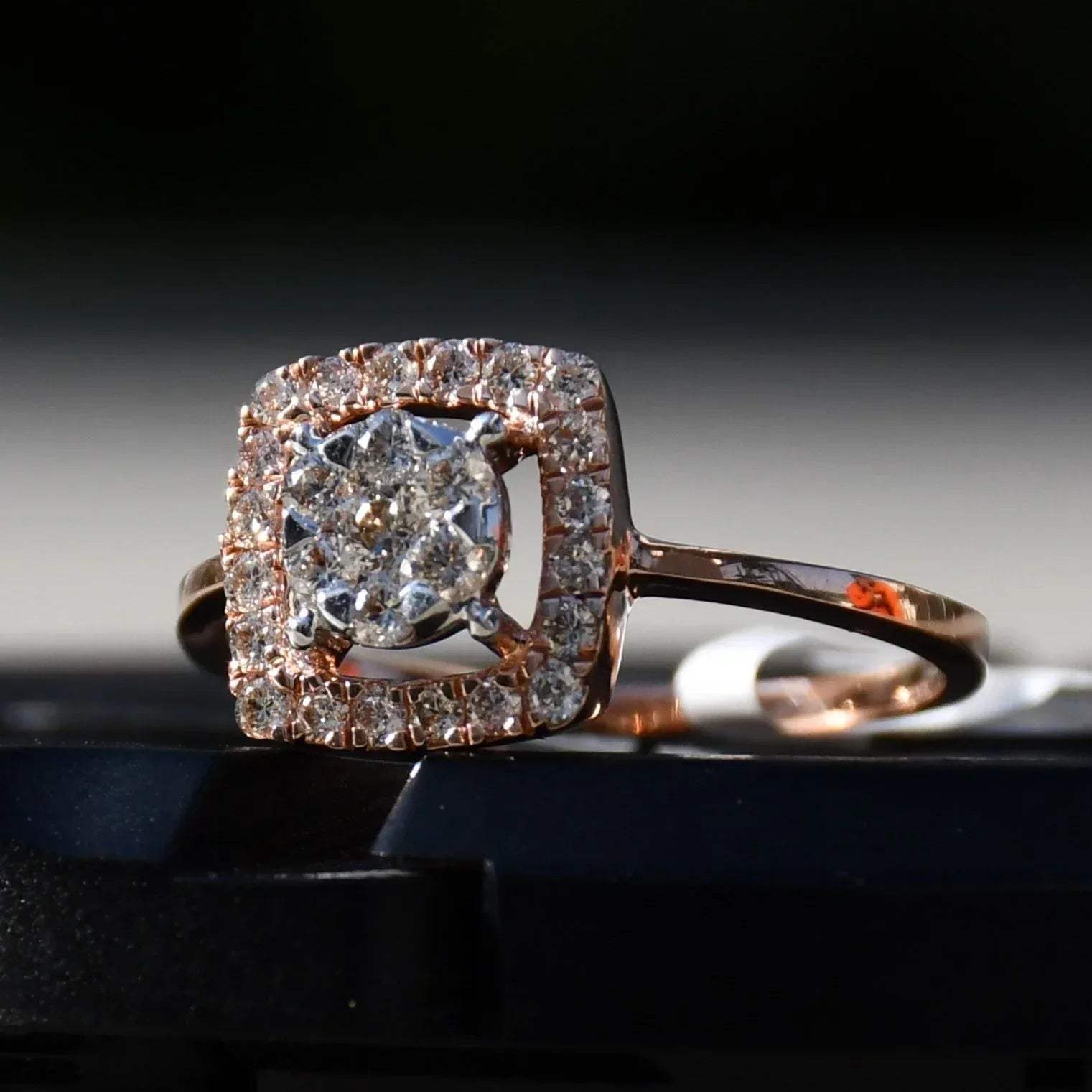 A gold band ring with a square-shaped, brilliant-cut diamonds centerpiece, set on a black surface.