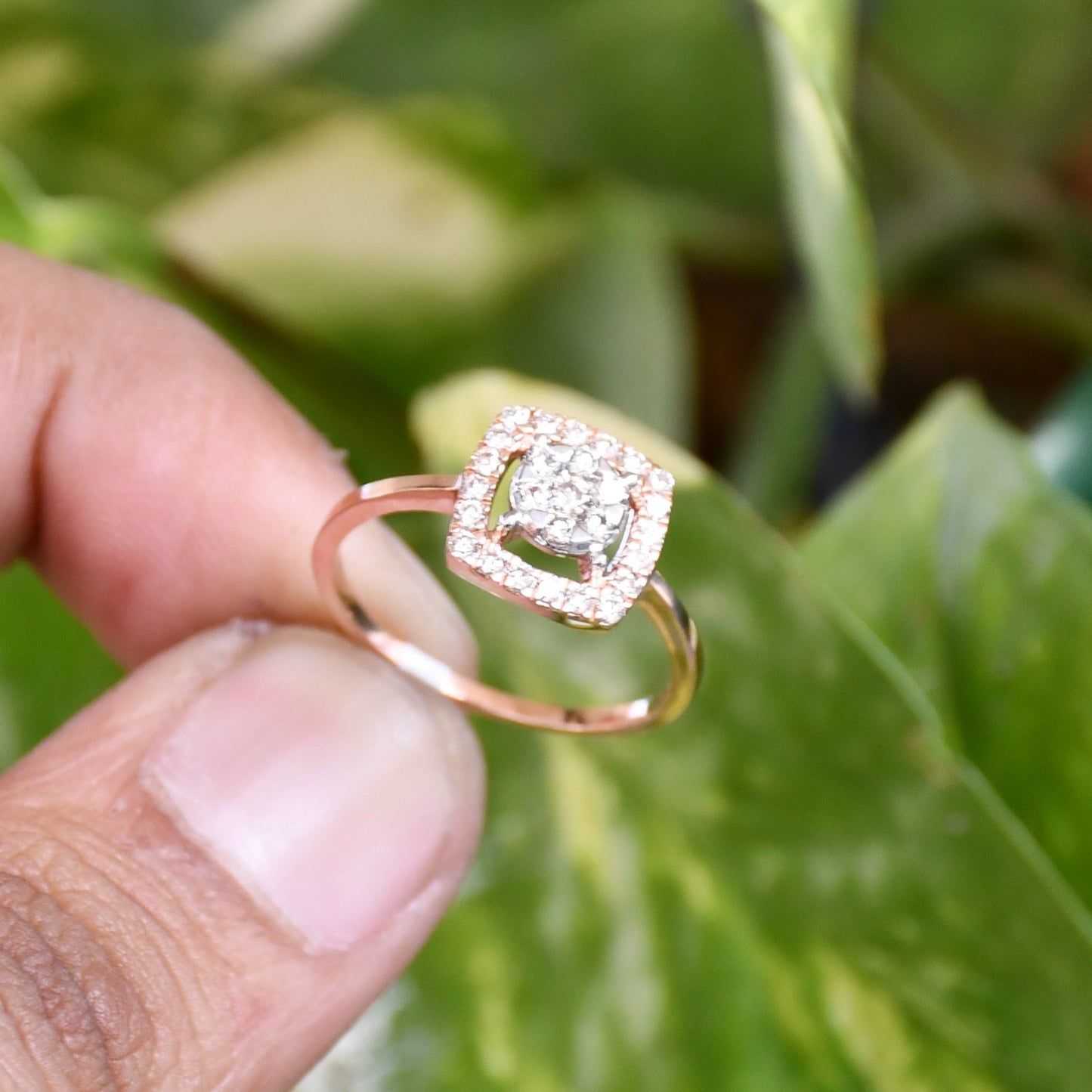 A gold band ring with a square-shaped, brilliant-cut diamonds centerpiece, hold by two fingers.