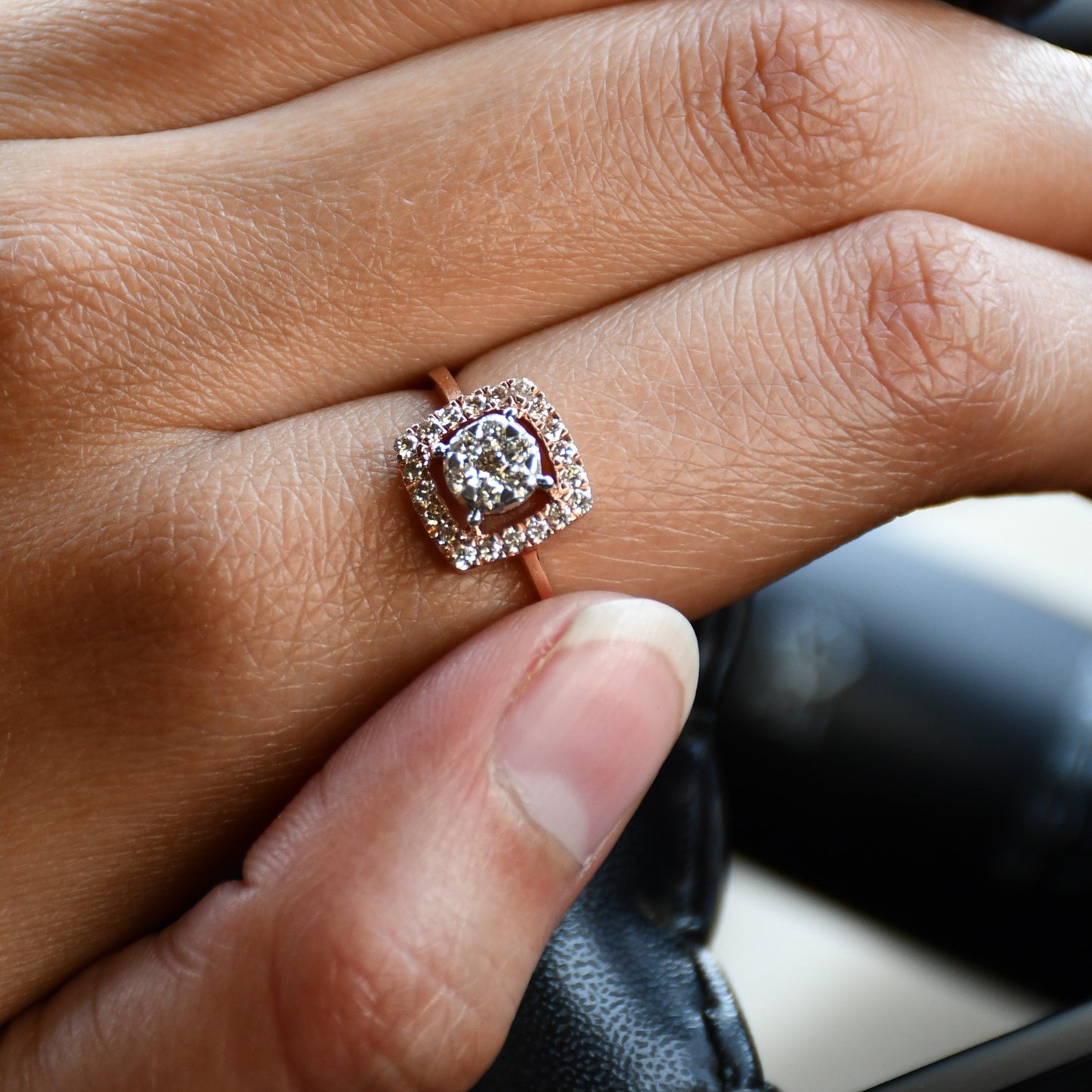 A gold band ring with a square-shaped, brilliant-cut diamonds centerpiece, displayed worn by a hand's finger.