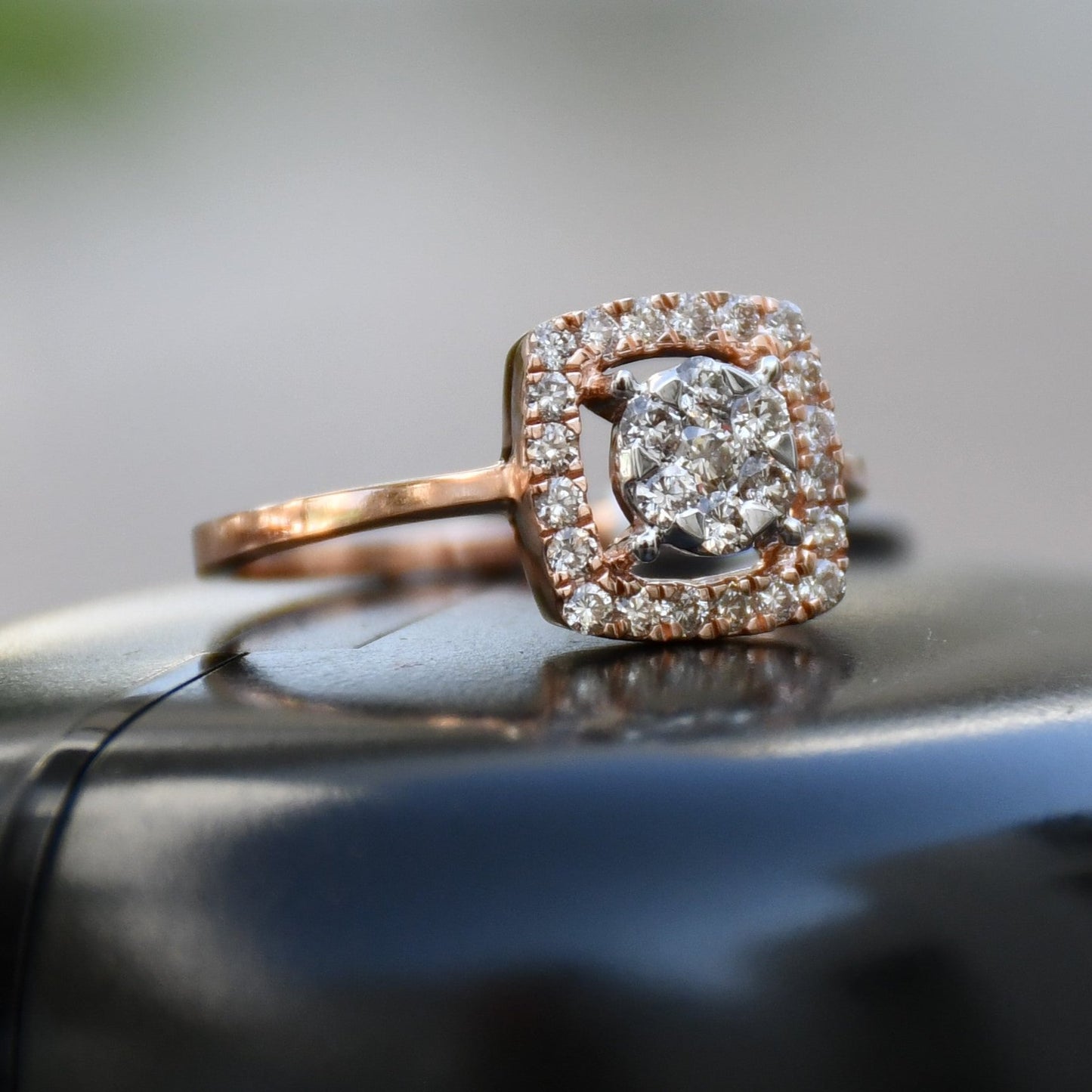 A gold band ring with a square-shaped, brilliant-cut diamonds centerpiece, set on a black surface.