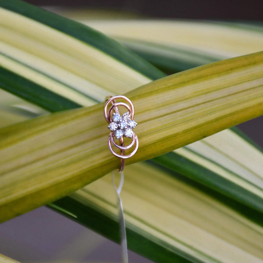 Delicate rose gold ring featuring a floral cluster of round diamonds at the center, showcased on green and yellow variegated leaves.