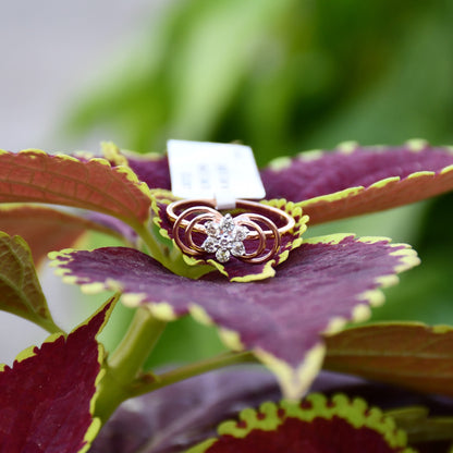 Delicate rose gold ring featuring a floral cluster of round diamonds at the center, showcased on a purple & yellow color leaf.