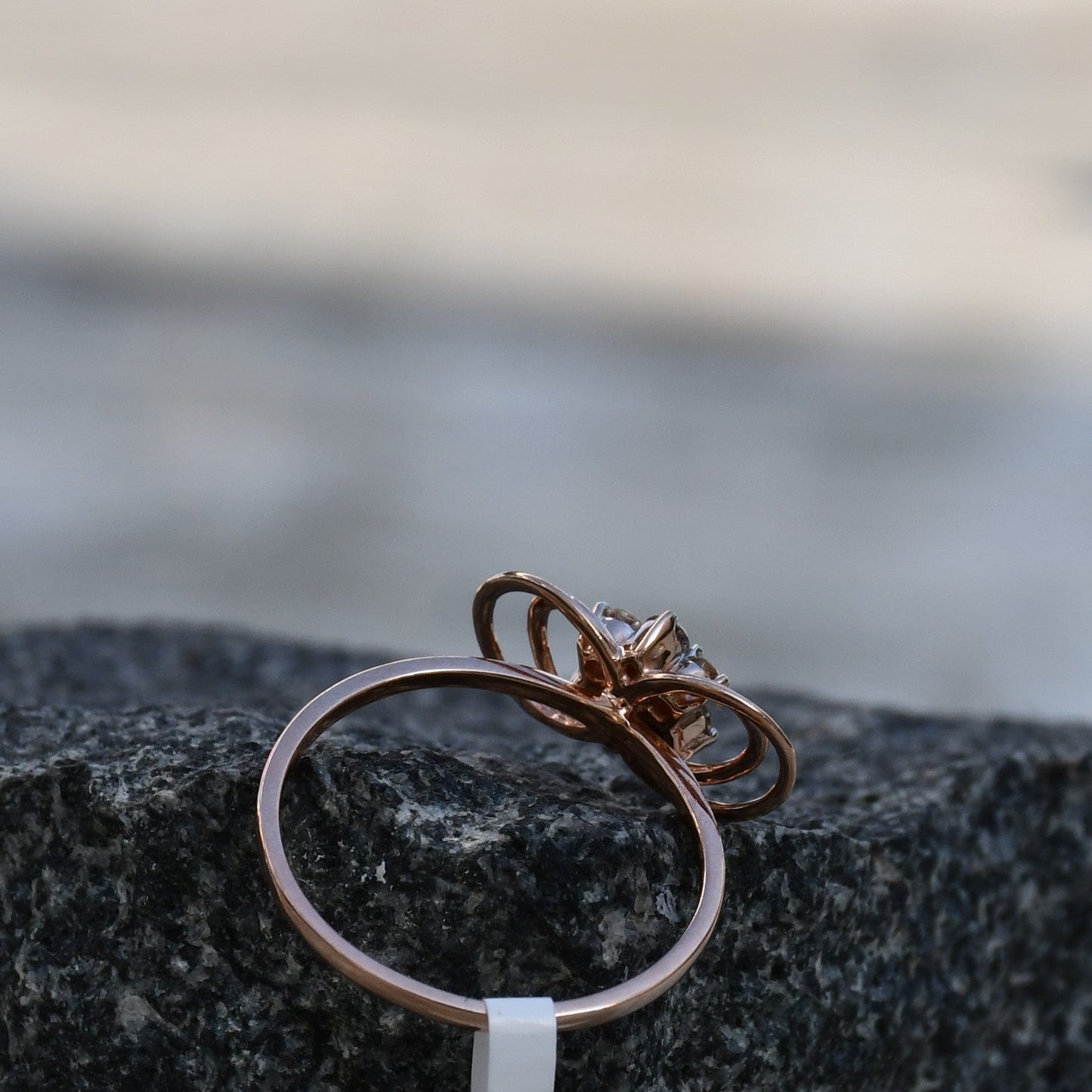 Delicate rose gold ring featuring a floral cluster of round diamonds at the center, showcased on a rough & textured surface.