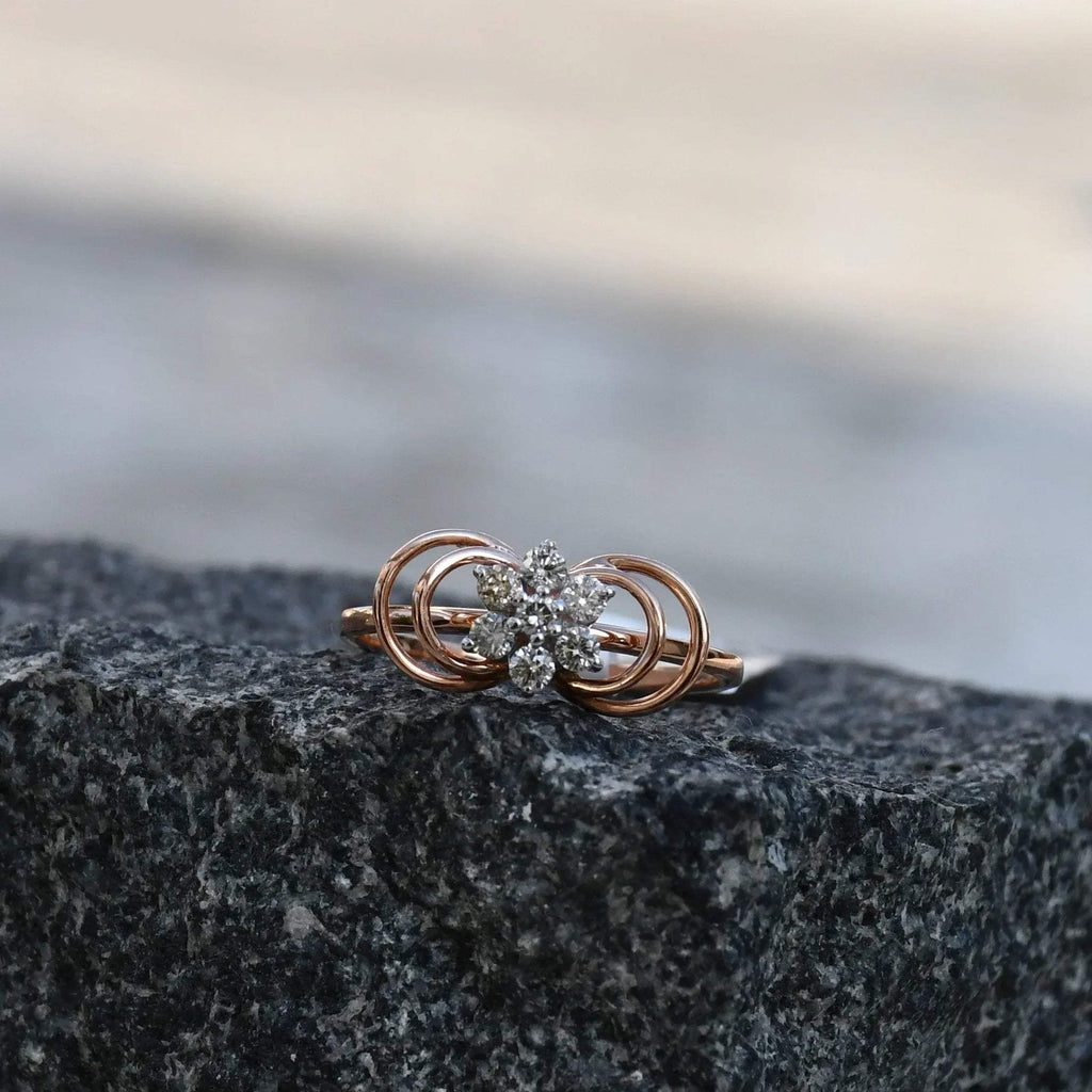 Delicate rose gold ring featuring a floral cluster of round diamonds at the center, showcased on a rough & textured surface.