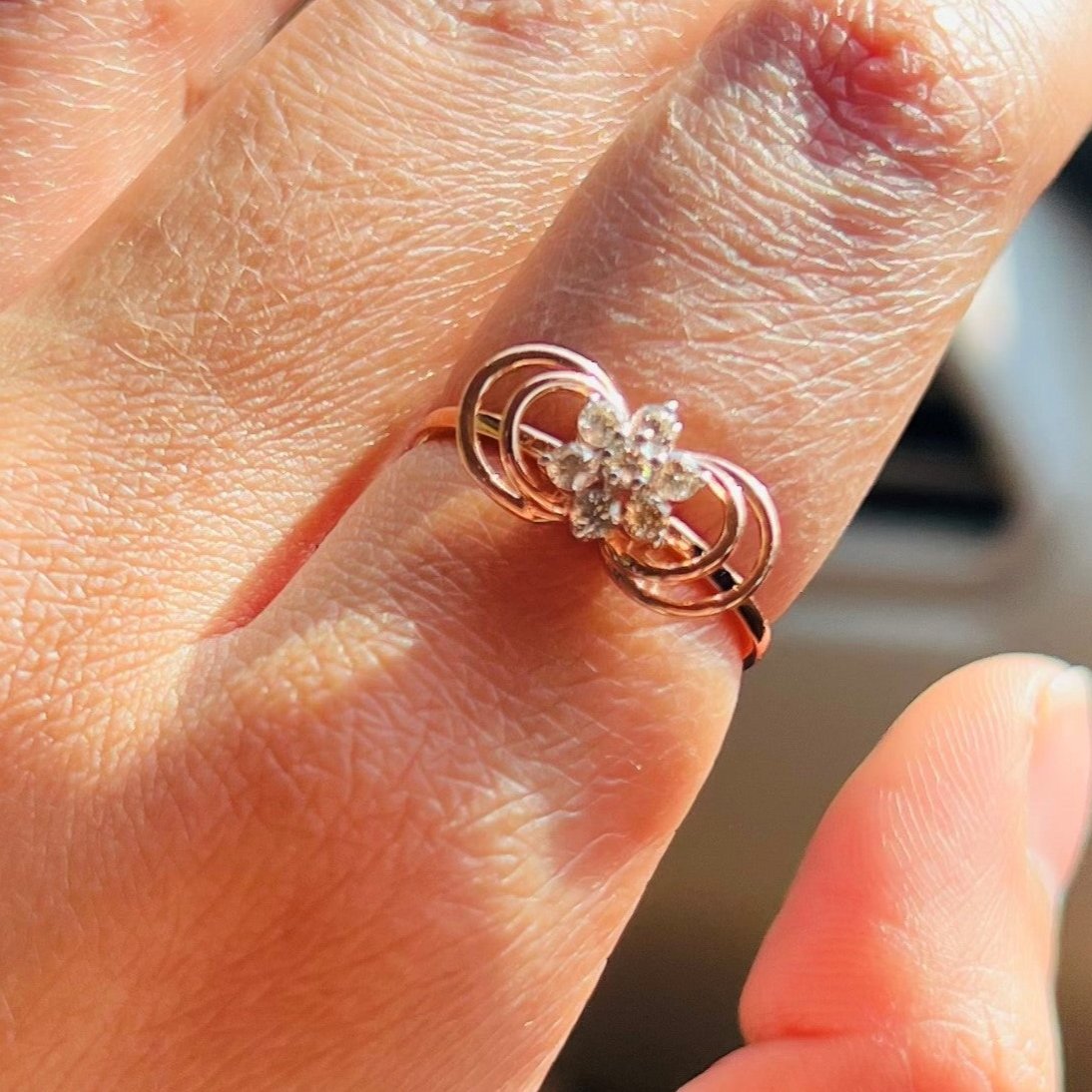 Delicate rose gold ring featuring a floral cluster of round diamonds at the center, showcased on a hand.