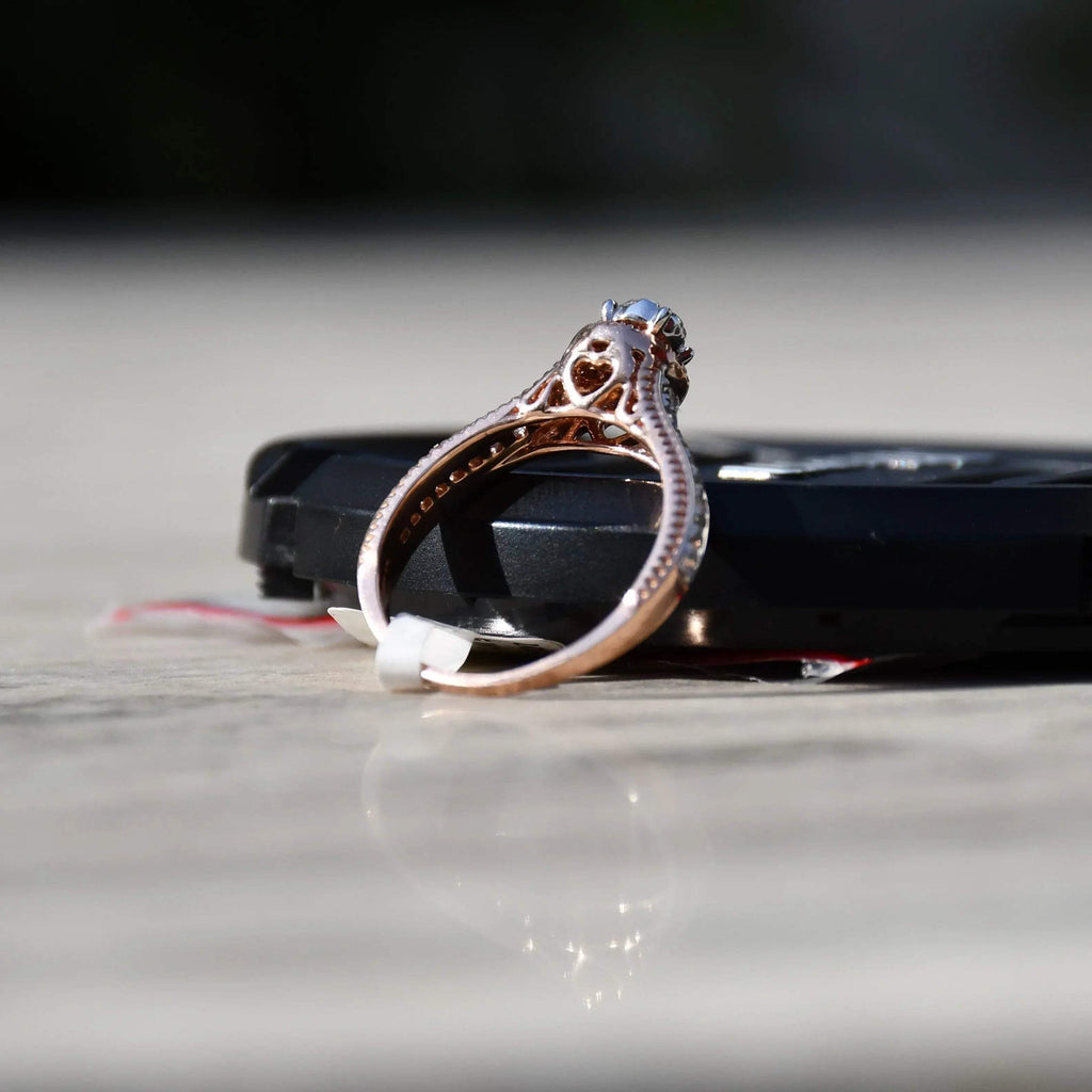 Close-up of a gold diamond ring displayed with the support of a black thing, featuring a round-cut center diamond surrounded by a delicate halo and a tapered band accented with small pavé-set diamonds and fine milgrain detailing.