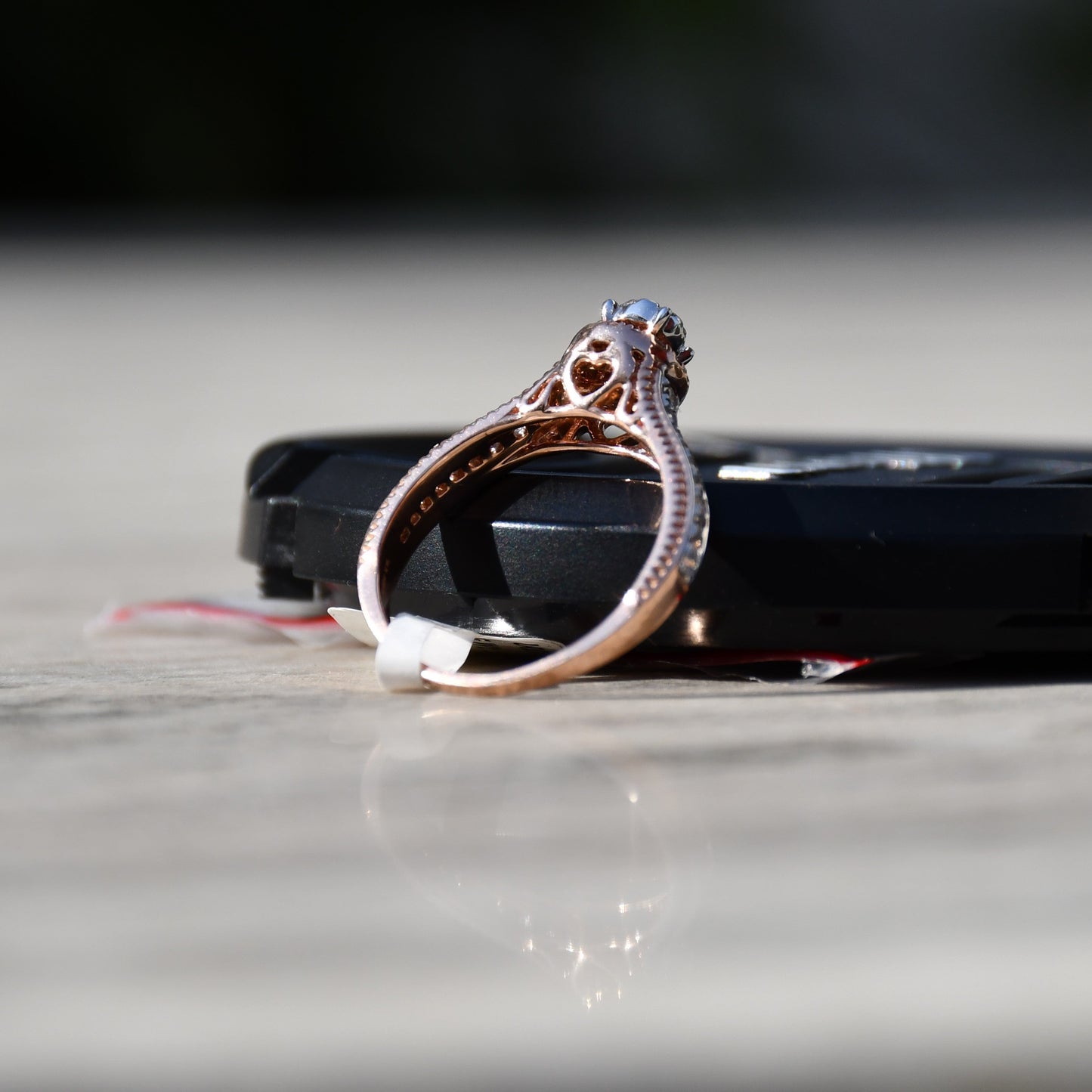 Close-up of a gold diamond ring displayed with the support of a black thing, featuring a round-cut center diamond surrounded by a delicate halo and a tapered band accented with small pavé-set diamonds and fine milgrain detailing.