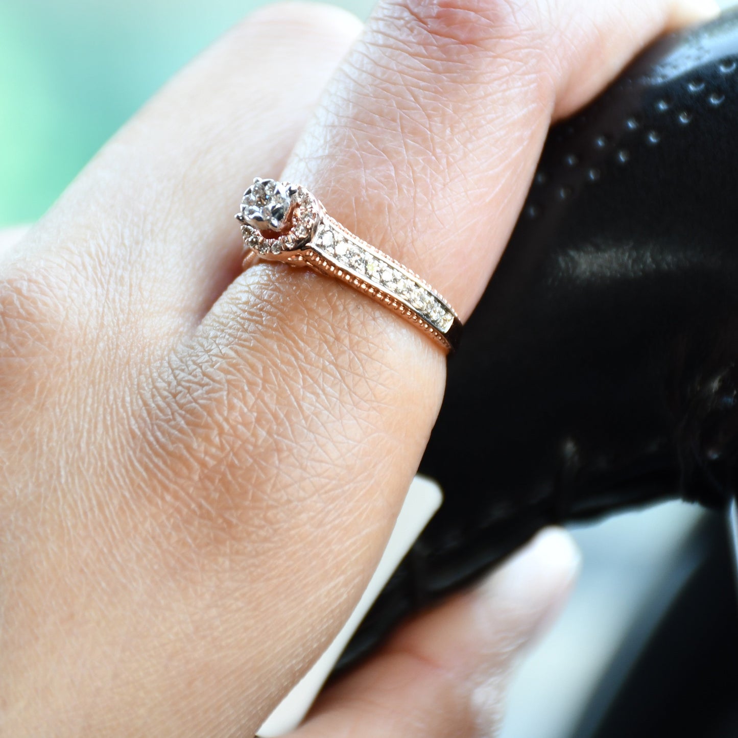 Close-up of a gold diamond ring worn on a finger, featuring a round-cut center diamond surrounded by a delicate halo and a tapered band accented with small pavé-set diamonds and fine milgrain detailing.