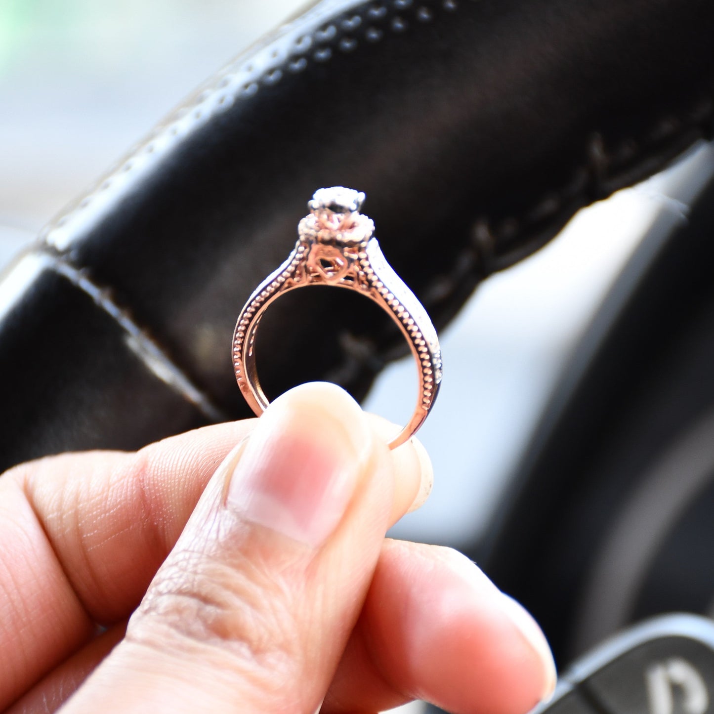 Close-up of a gold diamond ring holding with fingers, featuring a round-cut center diamond surrounded by a delicate halo and a tapered band accented with small pavé-set diamonds and fine milgrain detailing.