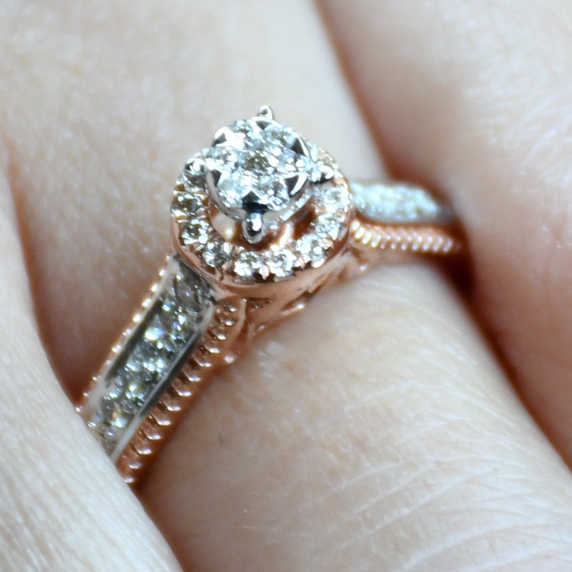 Close-up of a gold diamond ring worn on a finger, featuring a round-cut center diamond surrounded by a delicate halo and a tapered band accented with small pavé-set diamonds and fine milgrain detailing.