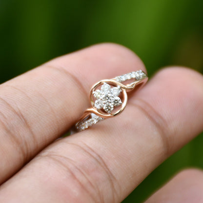 A person holding a 14k rose gold diamond ring with round brilliant cut diamonds in the center, surrounded by smaller clear diamonds.