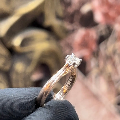A person's hand is showing a solitaire diamond ring against a natural background where diamond is set in prong setting.
