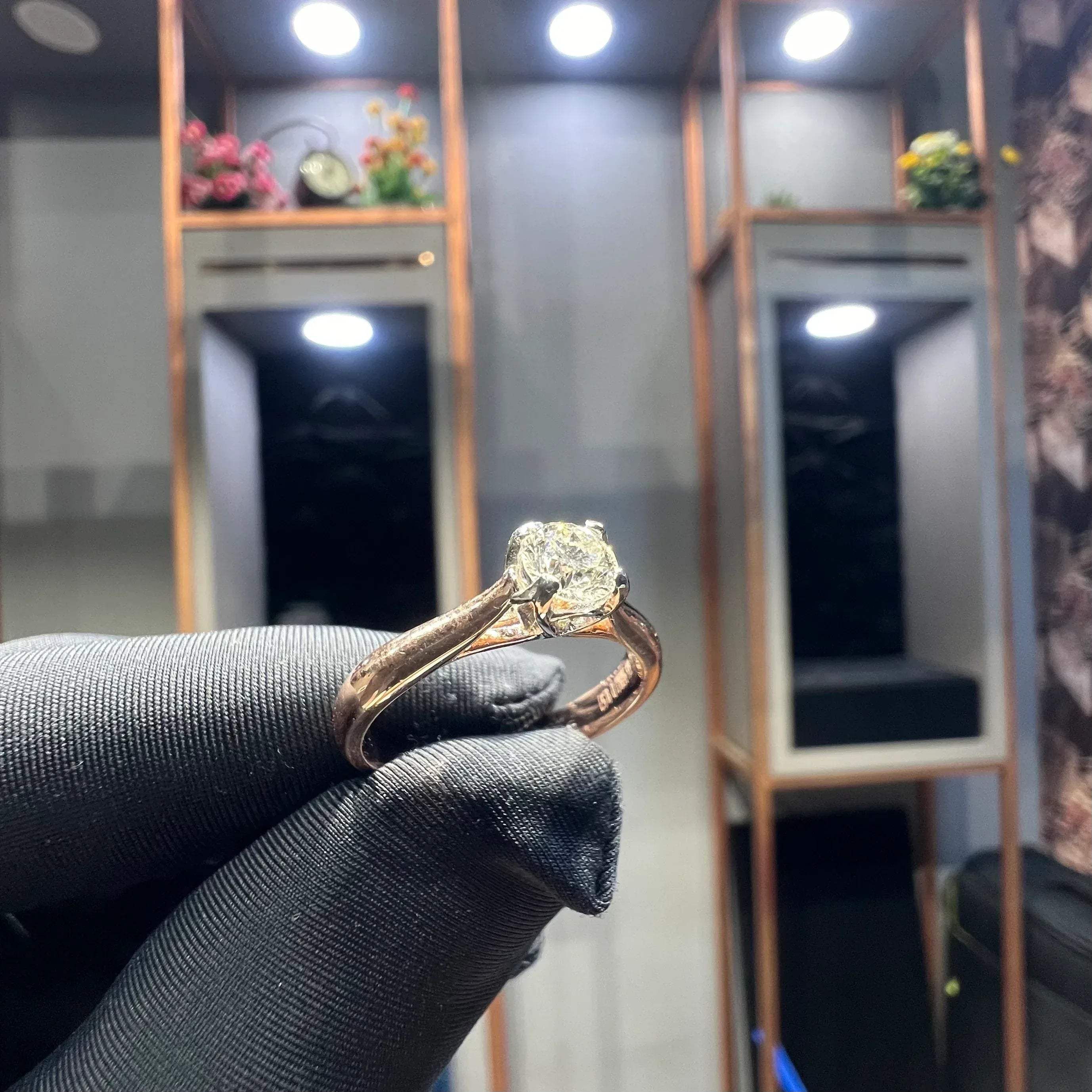 A person's hand is showing a solitaire diamond ring against a natural background where diamond is set in prong setting.