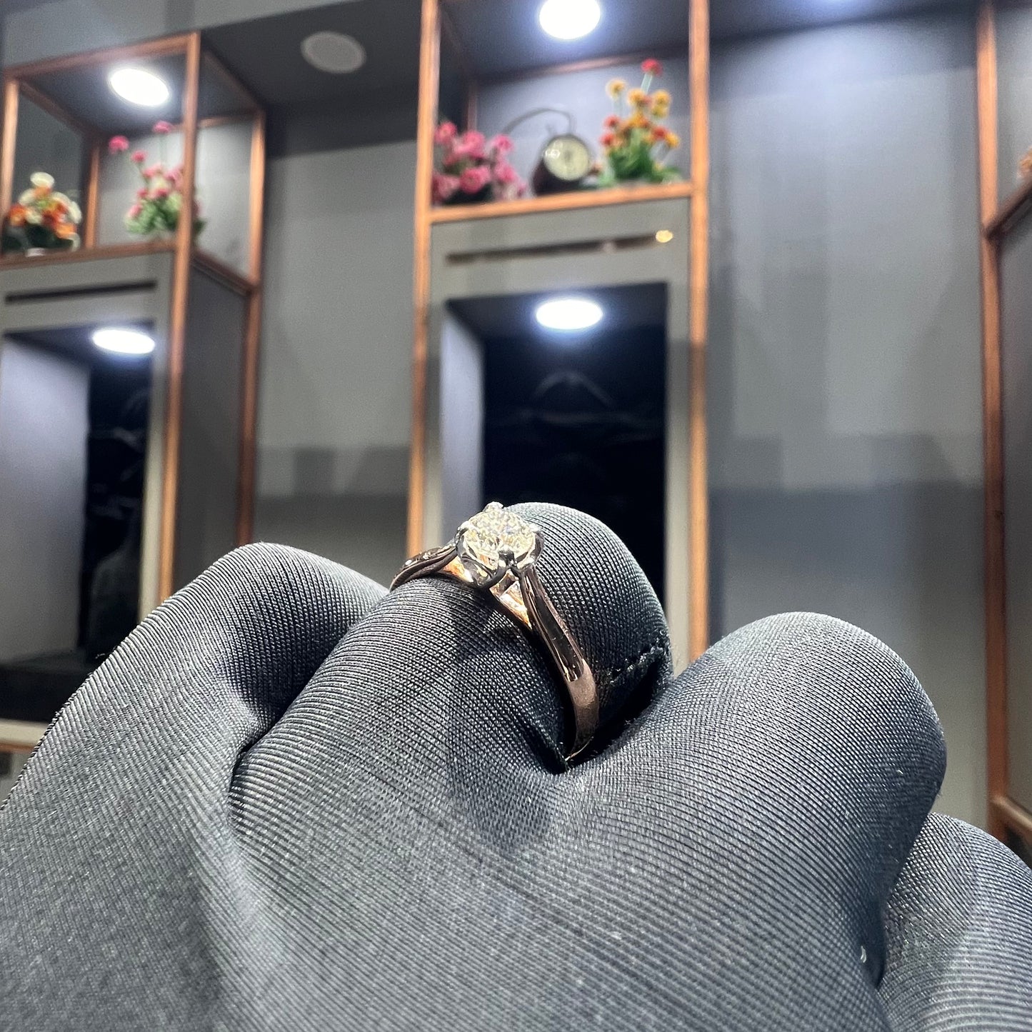 A person's hand is showing a solitaire diamond ring against a natural background where diamond is set in prong setting.