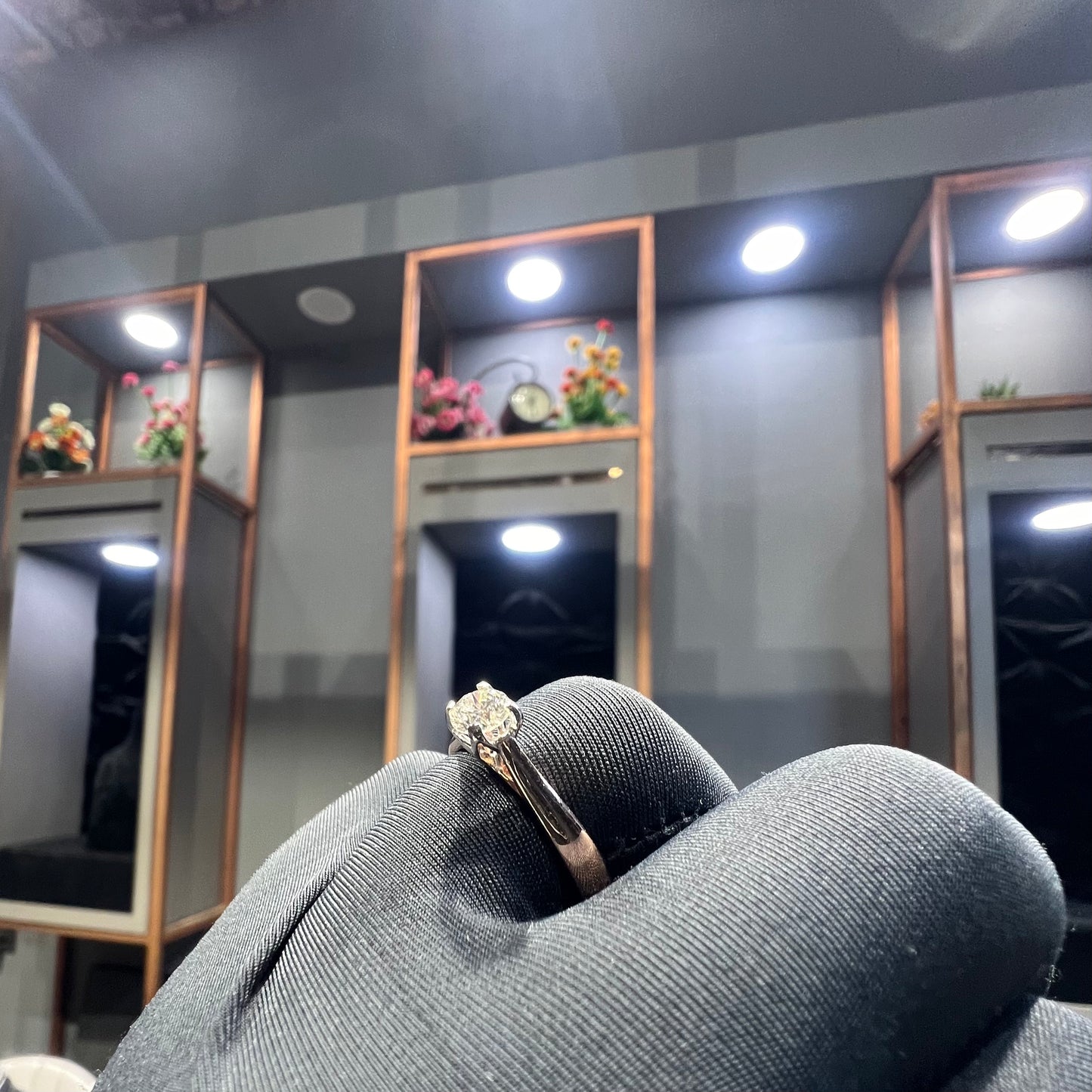 A person's hand is showing a solitaire diamond ring against a natural background where diamond is set in prong setting.