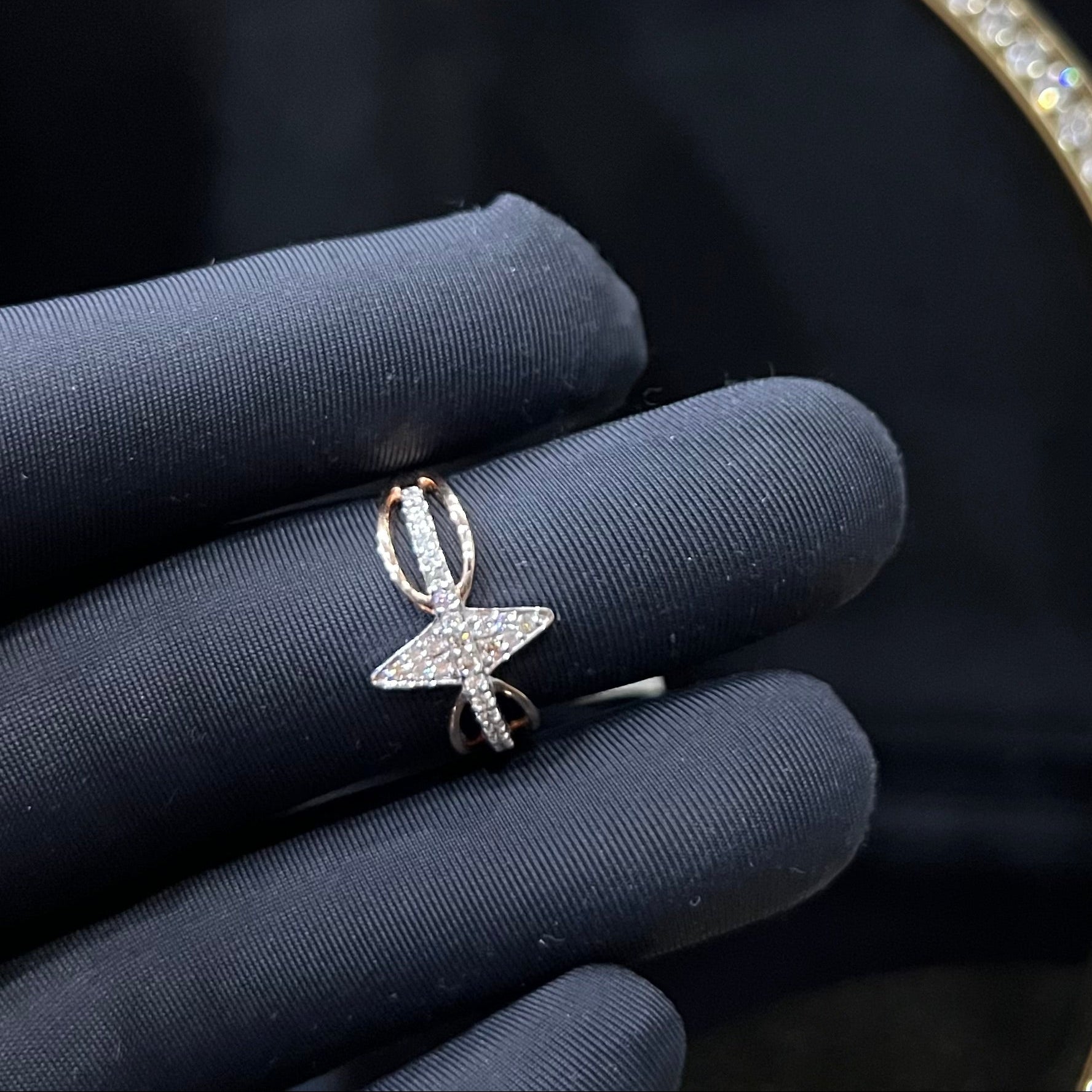 A handcrafted natural diamond solid gold ring, held in a gloved hand, featuring a brilliant cut diamond on a band with a star-shaped detail on the top.