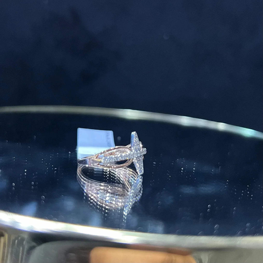 A handcrafted natural diamond solid gold ring, displayed on a reflective surface, featuring a brilliant cut diamond on a band with a star-shaped detail on the top.