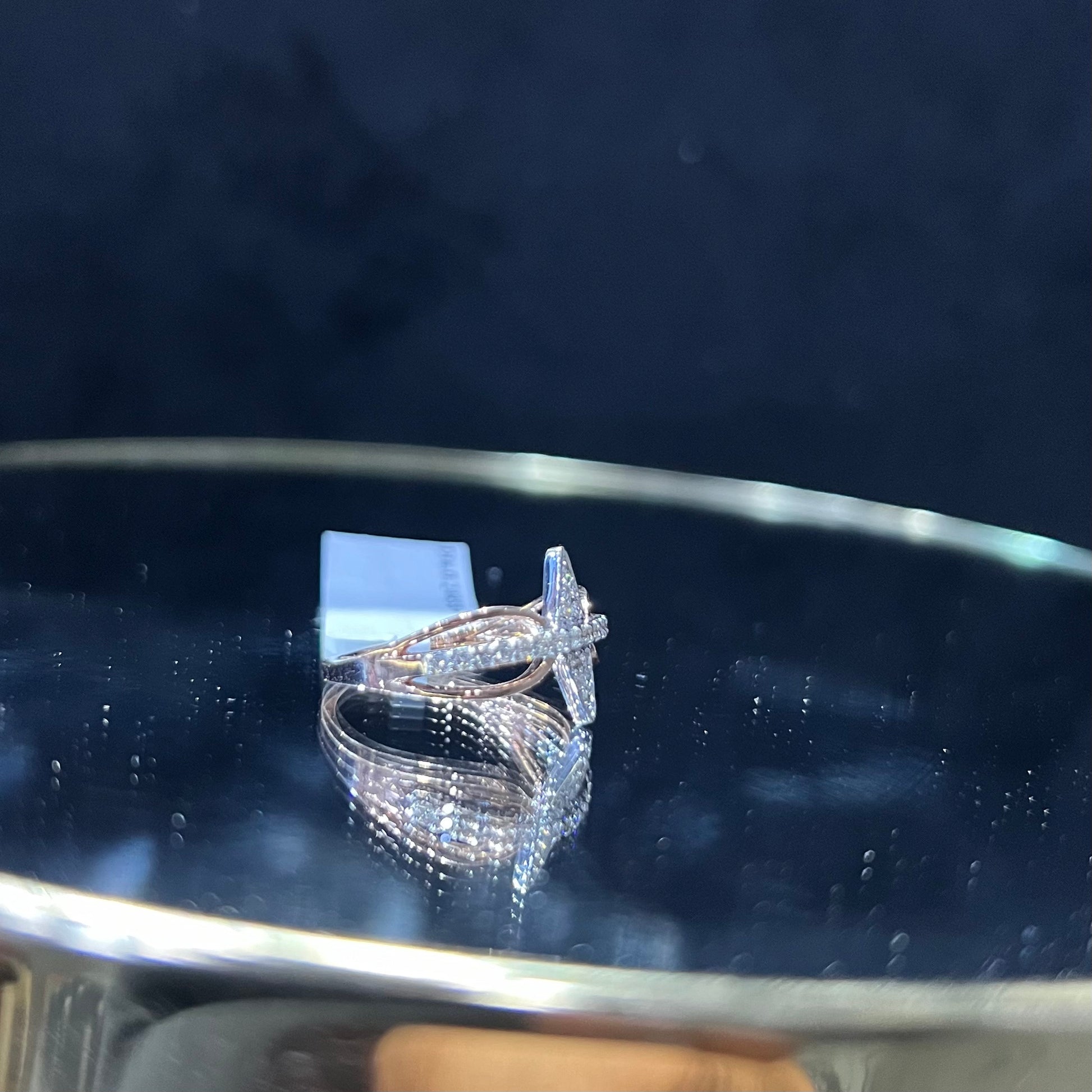 A handcrafted natural diamond solid gold ring, displayed on a reflective surface, featuring a brilliant cut diamond on a band with a star-shaped detail on the top.