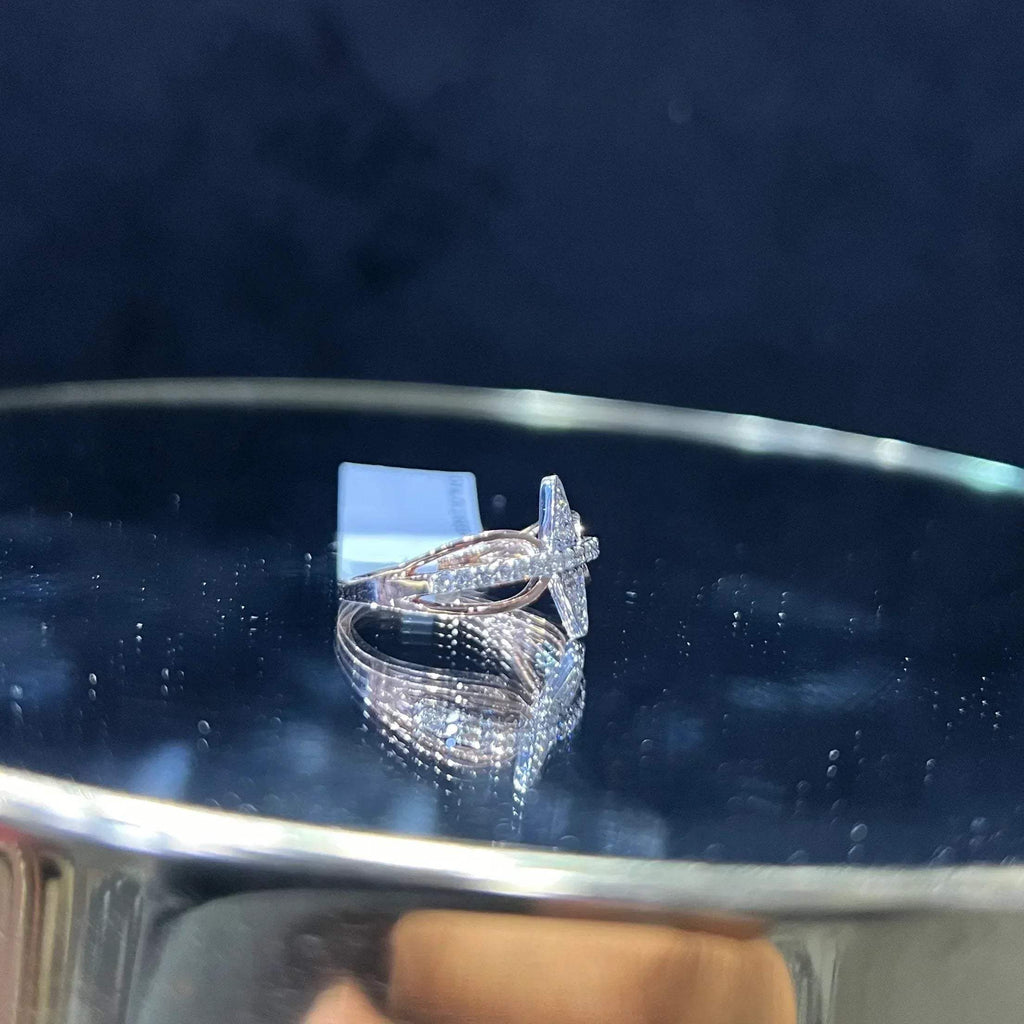 A handcrafted natural diamond solid gold ring, displayed on a reflective surface, featuring a brilliant cut diamond on a band with a star-shaped detail on the top.