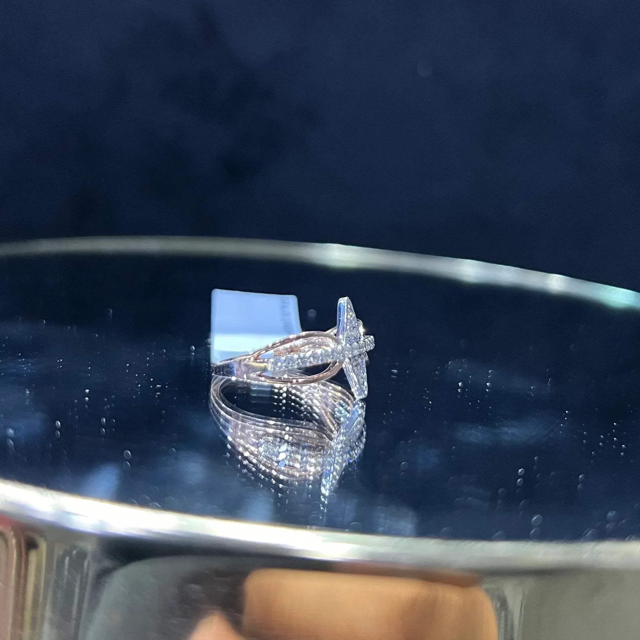 A handcrafted natural diamond solid gold ring, displayed on a reflective surface, featuring a brilliant cut diamond on a band with a star-shaped detail on the top.
