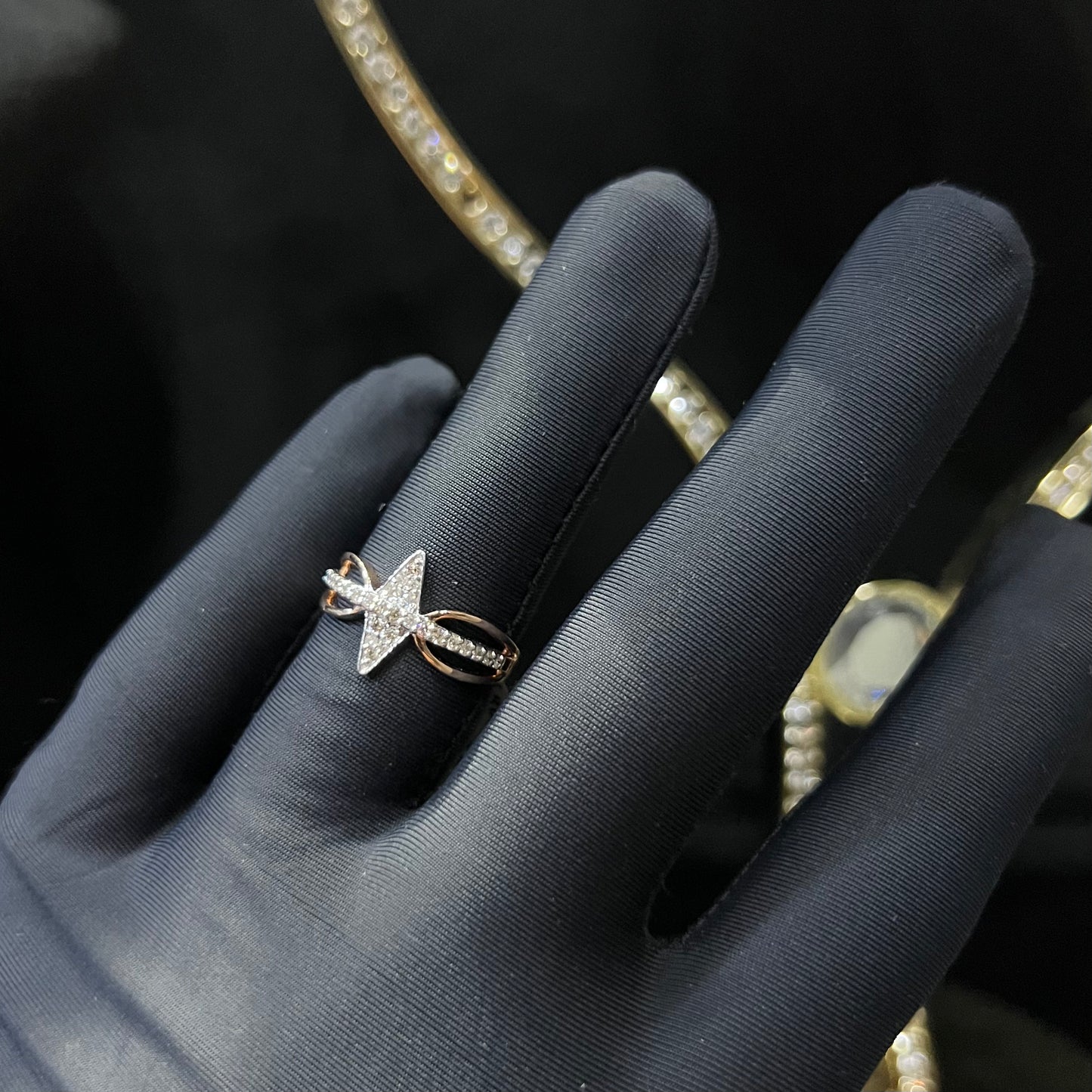 A handcrafted natural diamond solid gold ring, held in a gloved hand, featuring a brilliant cut diamond on a band with a star-shaped detail on the top.