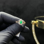 A handcrafted natural diamond solid gold ring, featuring a brilliant cut green stone centerpiece, surrounded by smaller clear diamonds, displayed by a black mannequin hand.