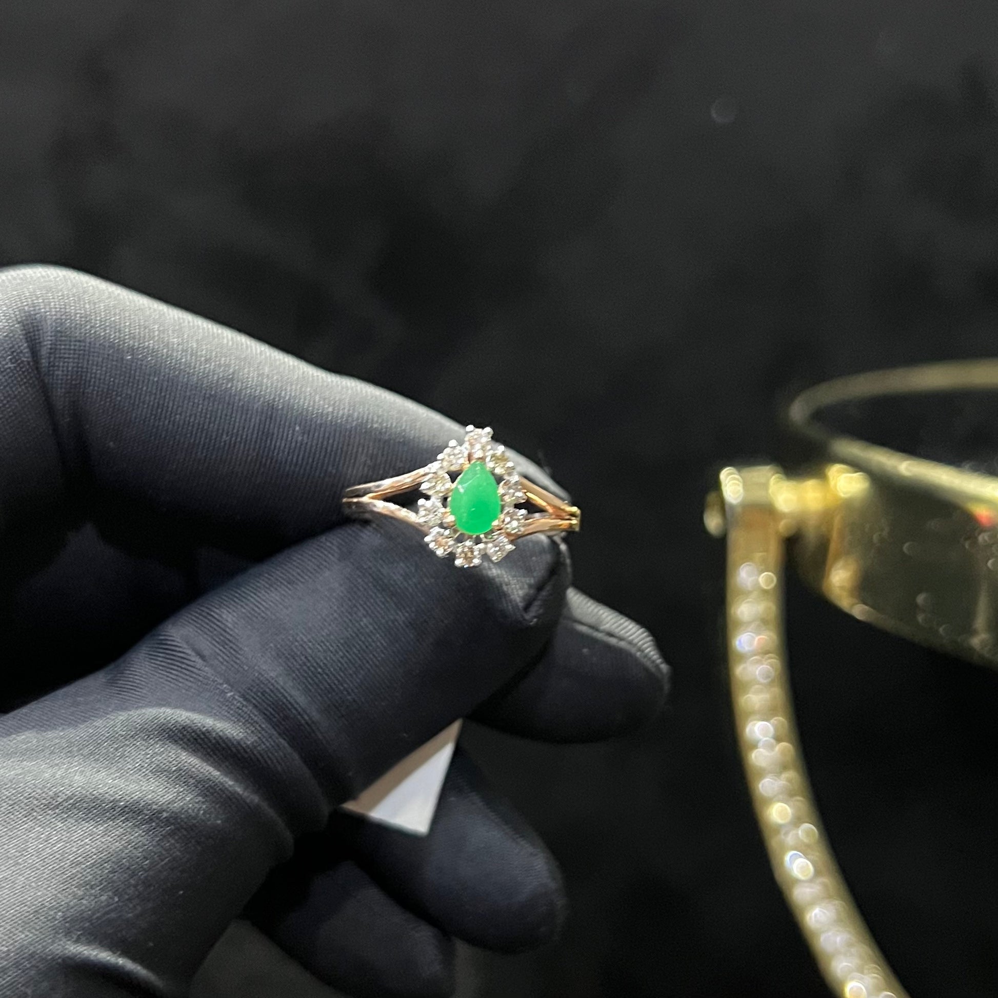 A handcrafted natural diamond solid gold ring, featuring a brilliant cut green stone centerpiece, surrounded by smaller clear diamonds, displayed by a black mannequin hand.