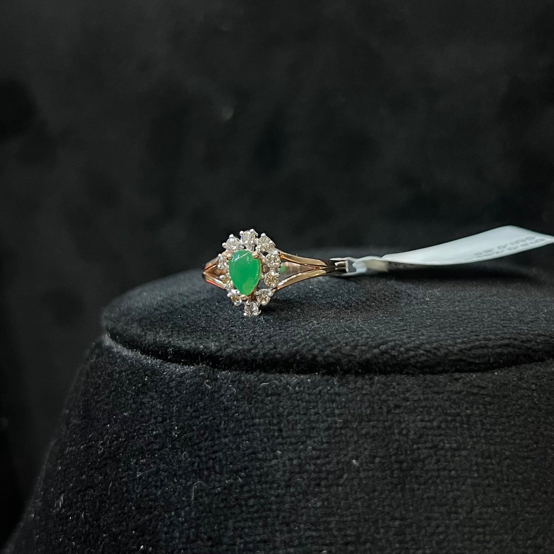 A handcrafted natural diamond solid gold ring, featuring a brilliant cut green stone centerpiece, surrounded by smaller clear diamonds, set on a black mannequin bust.