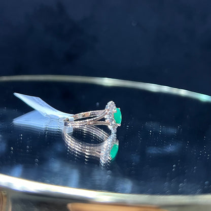 A handcrafted natural diamond solid gold ring, featuring a brilliant cut green stone centerpiece, surrounded by smaller clear diamonds, displayed on a reflective surface.