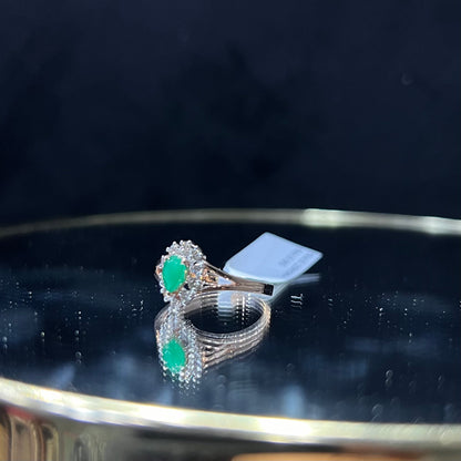 A handcrafted natural diamond solid gold ring, featuring a brilliant cut green stone centerpiece, surrounded by smaller clear diamonds, displayed on a reflective surface.