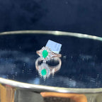 A handcrafted natural diamond solid gold ring, featuring a brilliant cut green stone centerpiece, surrounded by smaller clear diamonds, displayed on a reflective surface.