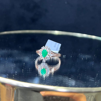 A handcrafted natural diamond solid gold ring, featuring a brilliant cut green stone centerpiece, surrounded by smaller clear diamonds, displayed on a reflective surface.