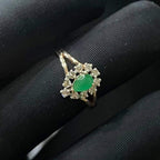 A handcrafted natural diamond solid gold ring, featuring a brilliant cut green stone centerpiece, surrounded by smaller clear diamonds, set on a black mannequin hand.