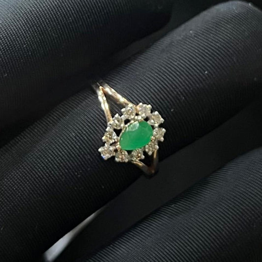 A handcrafted natural diamond solid gold ring, featuring a brilliant cut green stone centerpiece, surrounded by smaller clear diamonds, set on a black mannequin hand.