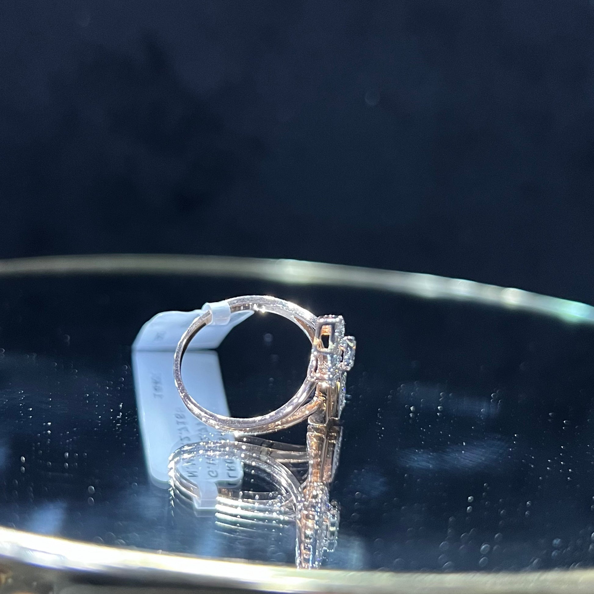 Elegant open-style diamond ring featuring a pear-shaped halo on one side and a square cluster on the other, worn in a black mannequin's hand displayed displayed against a reflective metallic background.